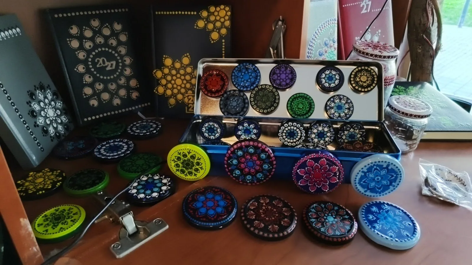 Agendas, piedras y tapas decoradas con puntillismo sobre la mesa del taller